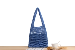 Blue hand-woven mesh tote bag with honeycomb knit detail on a light wood table