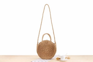 Detail of a round woven straw bag with spiral pattern on a white wooden background
