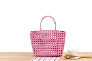 Close-up of pink woven PVC beach bag with a hollow grid design on light wood surface