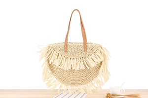 Detail of bohemian cream woven bag featuring long tassels and brown leather handles