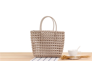 Close-up of beige PVC woven tote bag on a wooden table with home decor items