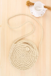 Close-up of circular hand-woven straw bag with spiral pattern on light wooden table