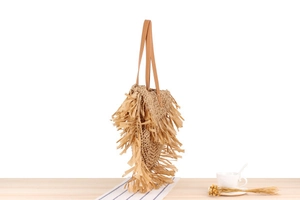 Detailed close-up of woven straw handbag with long raffia tassels and leather shoulder strap