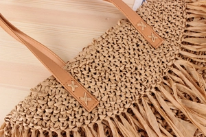 Detail of woven straw bag showing fringe edges and PU leather strap with X-shaped stitching