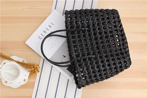 Detail shot of a black woven PVC tote bag on a wooden desk with lifestyle props