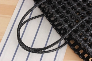 Detail of black PVC woven handbag featuring large mesh pattern and glossy round handles