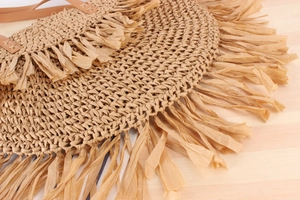 Detail of bohemian woven straw bag with paper tassels and brown leather shoulder strap