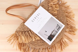 Detail of woven straw bag with long tassels and leather handle on a wood surface