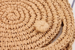 Detailed close-up of handmade round woven bag with natural raffia fibers and spherical clasp