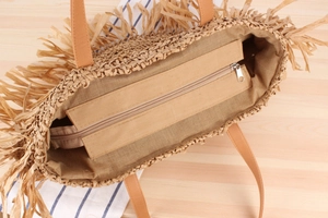 Close-up of woven straw tote bag with raffia tassels, leather straps and secure zipper