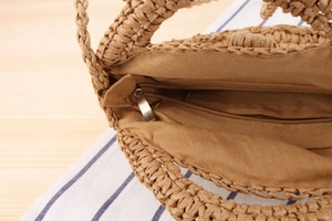 Detail view of the round woven straw bag showing the zipper closure and soft beige lining
