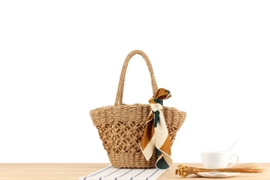 Close-up of woven straw handbag with hollow crochet pattern and decorative silk scarf