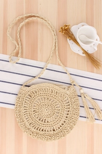 Detail view of round woven shoulder bag with hollow crochet pattern and wood bead tassel