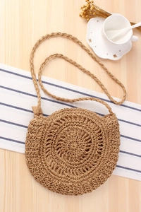 Detail of hand-woven round crossbody bag with spiral texture on light wood background