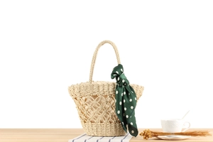 Detail view of a natural beige woven straw handbag with hollow mesh and silk scarf decoration