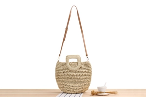 Detail of paper straw woven bag with brown leather strap and textured surface on table