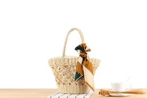 Detail of straw woven tote bag featuring cutout patterns and floral scarf handle