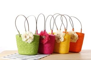 Detail of colorful woven straw tote bags with large 3D floral accents in vibrant summer colors