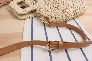 Detail of paper straw woven bag with brown PU leather strap and gold metal buckle