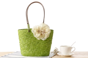Detail of green straw handbag with floral ornament on a wooden table with coffee cup