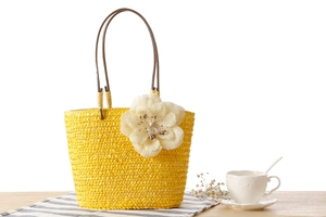 Detail of yellow straw bag with large white woven flower and brown handles