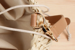 Detail of paper straw bucket bag featuring golden metal hardware and drawstring closure