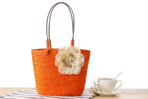 Close-up of bright orange straw tote bag featuring a large white 3D floral decoration