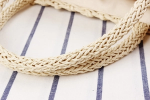 Close-up of a woven handle on a beige paper rope vacation bag with cotton linen lining