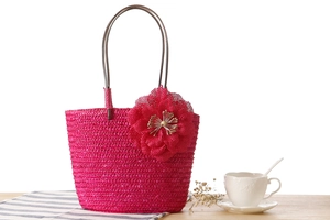 Detail of rose red straw woven handbag with mesh floral decoration on wooden table