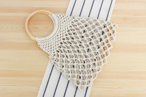Detailed macro view of woven macrame cotton rope beach bag with round wooden handle