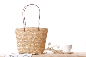 Close-up of woven straw tote bag with brown straps on a rustic wooden table setup
