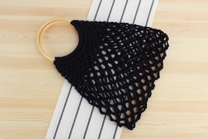 Detailed view of black handmade woven mesh bag with natural round wooden handles