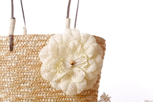 Close-up of handwoven straw bag with large decorative white flower and wooden beads