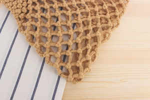 Detail of handcrafted brown woven net bag with thick cotton rope texture on wooden table