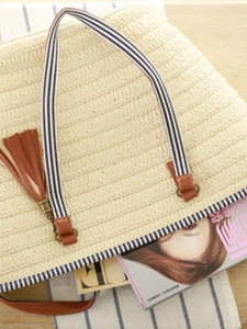 Minimalist woven straw beach tote bag with blue-white striped handles and tassel charm