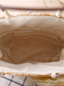 Top view of woven straw handbag with drawstring lining on a wooden and checkered surface