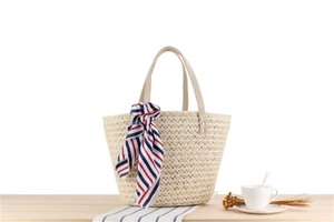 Detail of a woven straw beach tote bag with leather handles and striped silk scarf decor