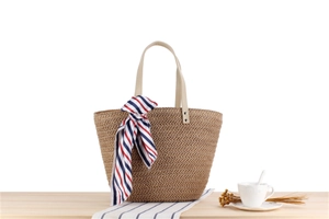 Detail of a woven straw tote bag with silk scarf and handle rivets on a table