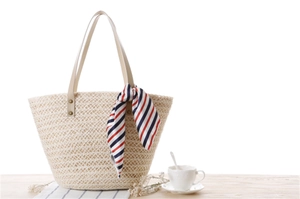Detail of a beige woven straw beach bag featuring a striped scarf and leather handles