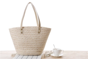 Detail of hollow-out straw woven tote bag with leather straps on a wooden table
