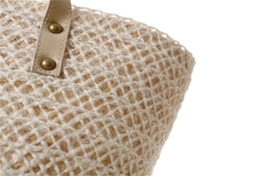 Close-up of woven straw handbag texture with beige leather handle and brass rivets