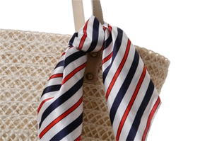 Detail of nautical striped silk scarf tied on woven straw bag with leather handles