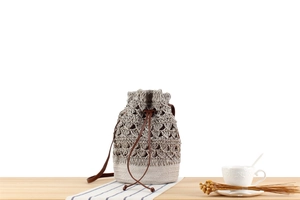 Detail of taupe woven straw bucket bag featuring hollow patterns and brown leather drawstrings