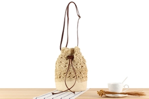 Detail of woven straw bucket bag with beige crochet hollow pattern and brown leather strap
