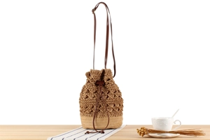 Detail of hollow-out woven straw bucket bag with leather drawstring and adjustable strap