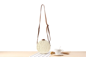 Detail of round straw crossbody bag with white woven texture and leather strap