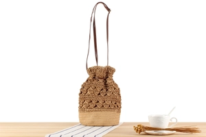 Detail of hollow paper rope weave texture and brown leather strap on bucket bag