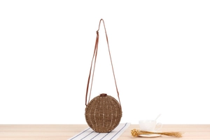 Detail view of round woven straw crossbody bag with brown leather clasp and shoulder strap
