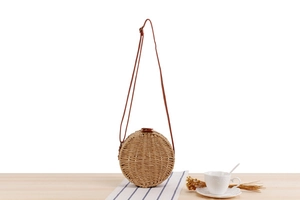 Detail of round straw crossbody bag with brown leather strap on minimalist wooden table