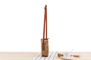 Side view of round woven straw crossbody bag with brown leather strap and metal buckle